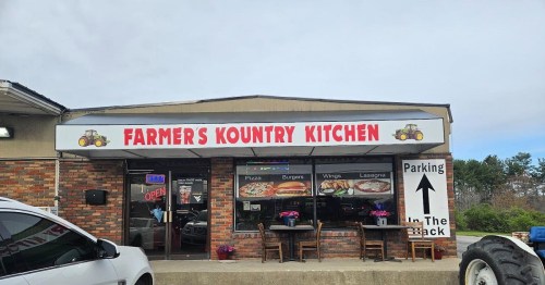 Exterior of Farmer's Kountry Kitchen, featuring a sign with menu items and a parking direction. Cloudy sky above.