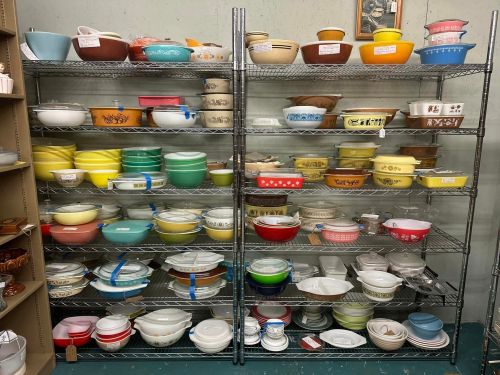 A display of colorful vintage bowls and dishes arranged on metal shelves in a store.