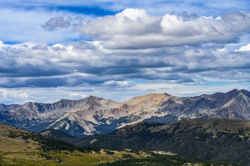 A panoramic view of rugged mountains under a cloudy sky, with green valleys in the foreground.