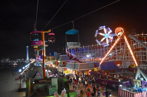 A vibrant amusement park at night, featuring a Ferris wheel, rides, and colorful lights along a bustling boardwalk.
