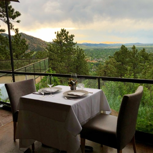 A table set for two with a scenic view of mountains and valleys under a cloudy sky.