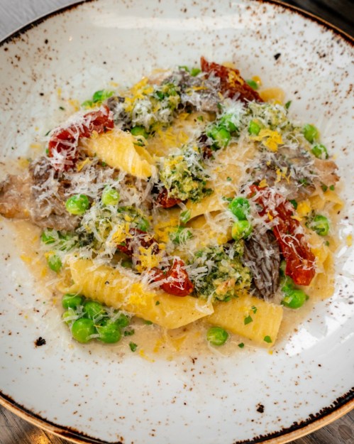 A plate of pasta with green peas, sun-dried tomatoes, and a creamy sauce, topped with grated cheese and herbs.