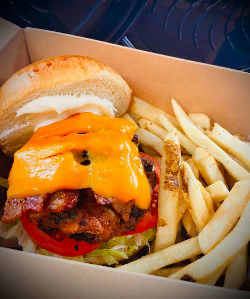 A delicious burger with melted cheese, lettuce, and tomato, served with a side of golden fries in a takeout box.