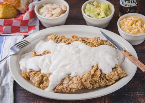 A plate of fried chicken smothered in white gravy, served with sides of macaroni, salad, and sliced apples.
