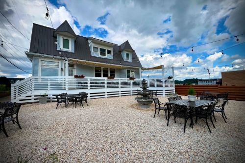 A charming house with a patio area, surrounded by gravel and outdoor seating, under a cloudy sky with string lights.