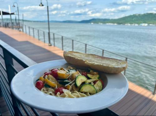 A plate of pasta with vegetables and garlic bread, overlooking a scenic waterfront view.