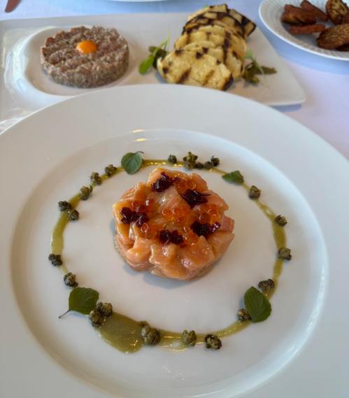 A gourmet dish featuring salmon tartare topped with caviar, surrounded by a green sauce and garnished with herbs.
