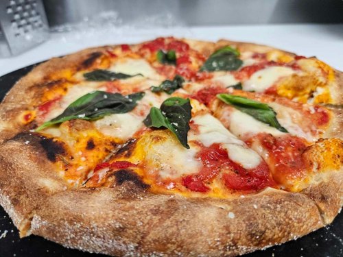 A freshly baked pizza topped with mozzarella, tomato sauce, and fresh basil on a black stone surface.