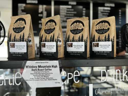 Three bags of Cody Coffee's "Whiskey Mountain High" dark roast on display, with a sign detailing the coffee's features.