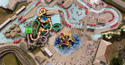 Aerial view of a vibrant water park featuring slides, pools, and lounging areas filled with colorful umbrellas and visitors.