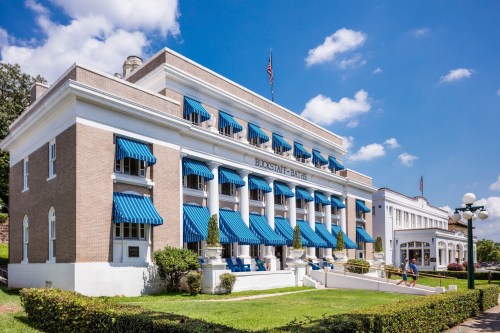 Historic building with blue awnings, American flags, and landscaped grounds under a bright blue sky.