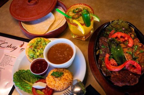 A vibrant Mexican meal featuring grilled meats, rice, beans, guacamole, tortillas, and a colorful margarita.