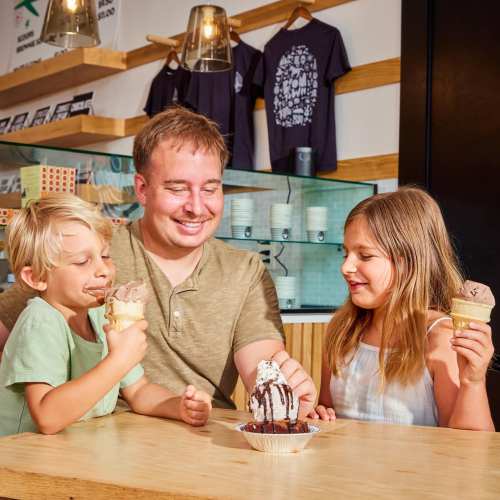 A man and two children enjoy ice cream cones and a sundae at a cozy café, smiling and sharing a joyful moment.