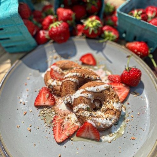 A plate of chocolate donuts topped with cream and fresh strawberries, surrounded by more strawberries in baskets.