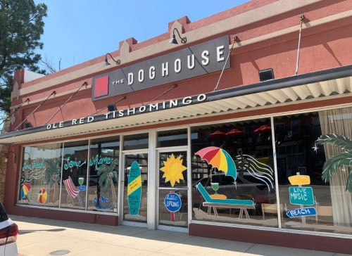 Exterior of The Doghouse restaurant with colorful signage, featuring beach themes and live music announcements.