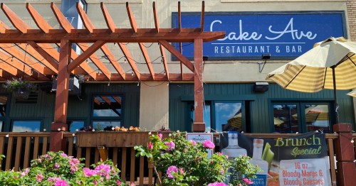 Exterior view of Lake Ave Restaurant & Bar with a wooden pergola, flowers, and a sign promoting brunch specials.