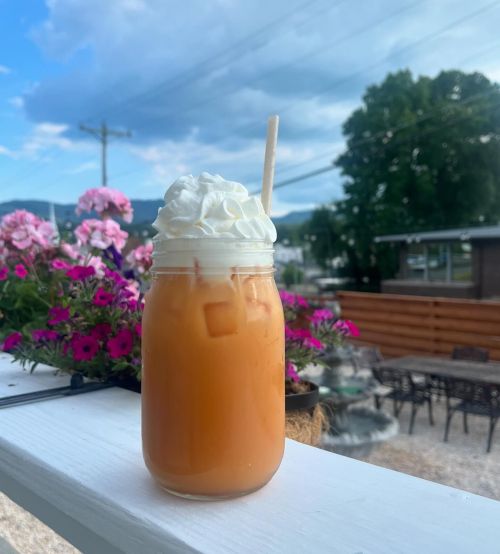 A glass of iced drink topped with whipped cream, set against a backdrop of flowers and a scenic outdoor view.