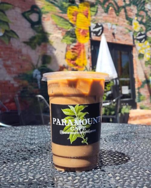 A cup of iced coffee sits on a table, with a colorful mural of flowers and butterflies in the background.