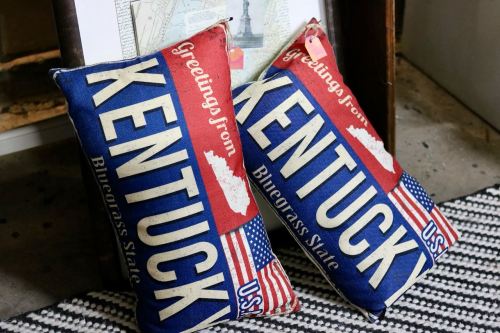 Two decorative pillows featuring "Greetings from Kentucky" and the phrase "Bluegrass State" with American flag designs.