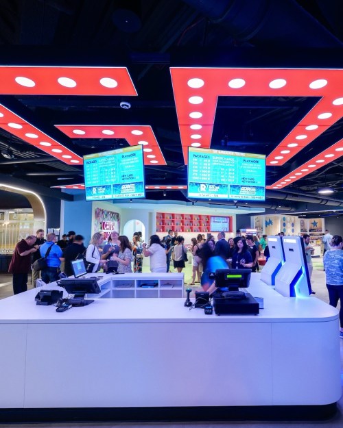 A busy retail space with a modern checkout area, bright signage, and a crowd of shoppers in the background.