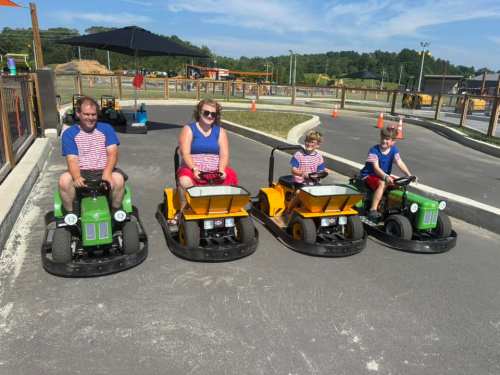 Four people in go-karts on a track, smiling and wearing matching outfits, with a sunny outdoor setting in the background.