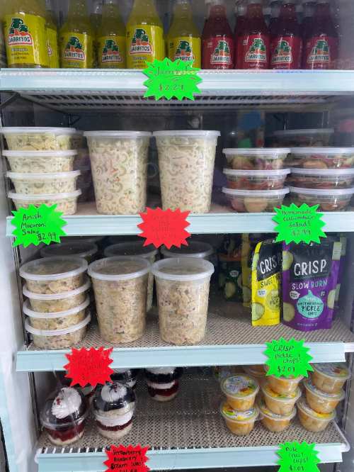 A display case filled with various snacks, salads, and drinks, labeled with prices and colorful tags.