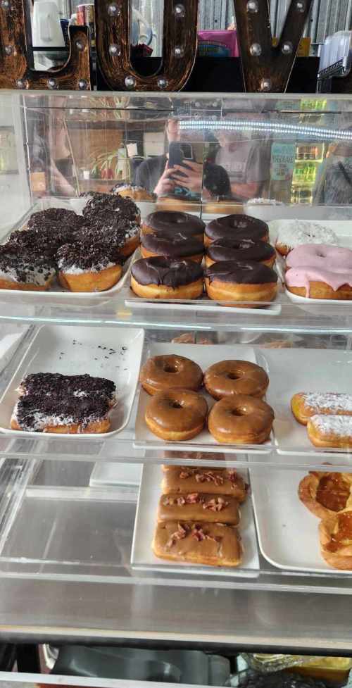 A display case filled with various donuts, including chocolate, pink frosted, and glazed options.