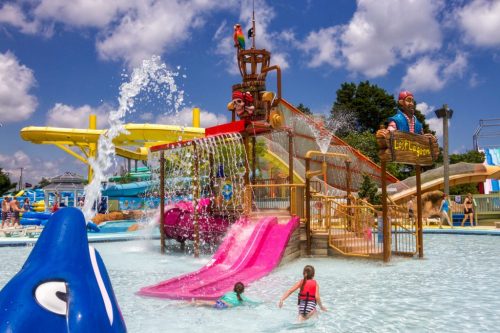 A vibrant water park scene with colorful slides, kids playing in the water, and a pirate-themed play structure.