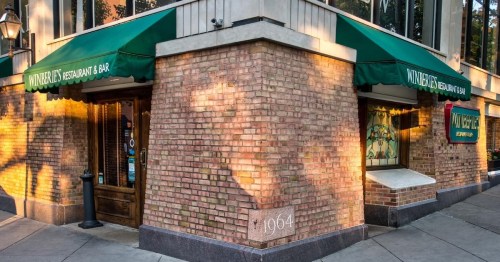 Exterior of a restaurant with green awnings, brick walls, and a sign displaying "1964" at the corner of the building.