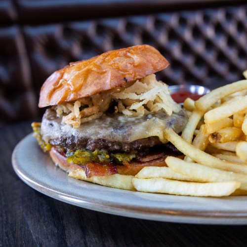 A close-up of a burger topped with crispy onions, pickles, and cheese, served with a side of golden French fries.