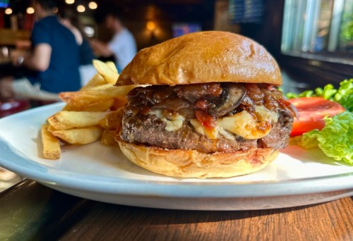 A juicy burger with melted cheese, sautéed mushrooms, and caramelized onions, served with fries and fresh vegetables.