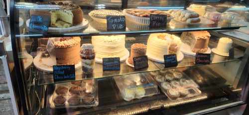 A display case filled with various cakes and pies, including cheesecake, cherry pie, and chocolate desserts.