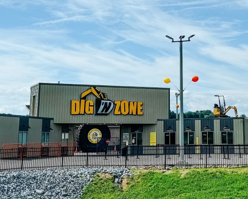 A building with the sign "DIG IN ZONE," featuring construction equipment and colorful balloons outside.
