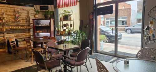 Cozy café interior with wooden decor, tables, chairs, and a large window showing a street view outside.