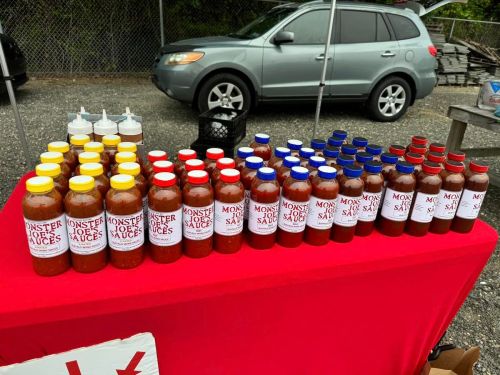 A table displaying various bottles of Monster Joe's sauces in yellow, red, and blue, set up at an outdoor market.