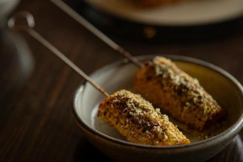 Grilled corn on skewers, seasoned and served on a small plate, with a dark wooden background.
