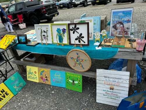 A display table at a market featuring colorful artwork, signs, and crafts, with a variety of decorative items.