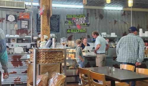 A cozy café interior with customers ordering at the counter, rustic decor, and a display of baked goods.