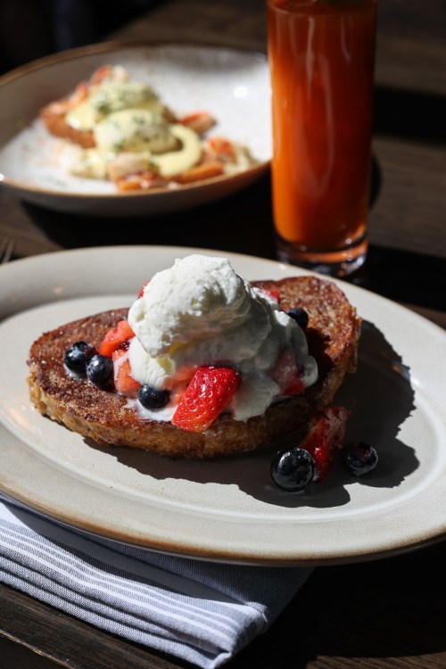 A plate of French toast topped with whipped cream and fresh berries, with a glass of juice in the background.
