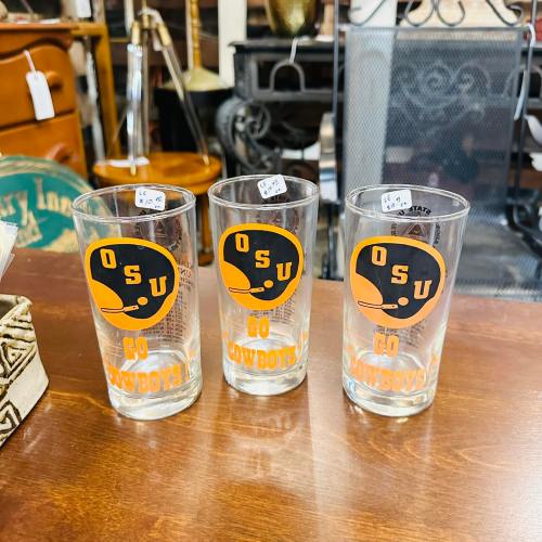 Three clear glasses with orange and black "OSU Go Cowboys" logos on a wooden table. Price tags visible on each glass.