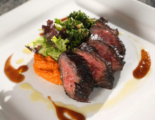 A plate featuring sliced steak, vibrant greens, and a swirl of orange puree, garnished with sauce.