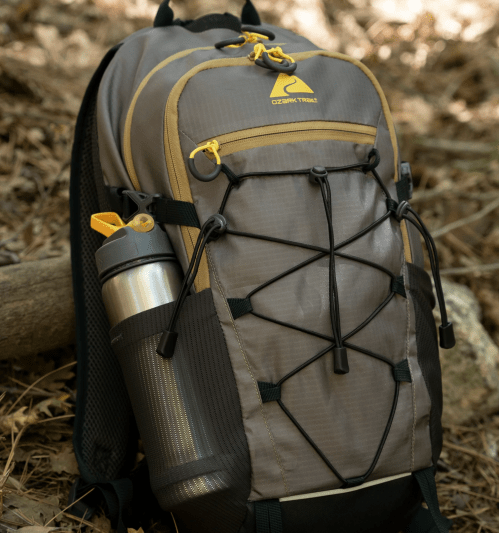 A gray and yellow backpack with a water bottle attached, set against a natural, wooded background.