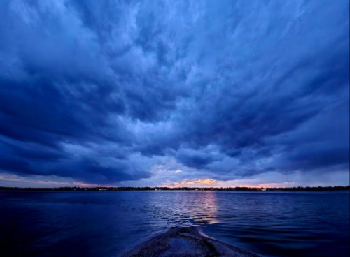 A serene lake at dusk, with dramatic blue clouds reflecting on the water and a hint of sunset on the horizon.