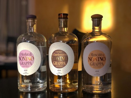Three bottles of grappa labeled Merlot, Chardonnay, and Moscato, each with distinct designs and colors.