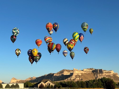 A vibrant display of colorful hot air balloons soaring against a clear blue sky, with a scenic landscape in the background.