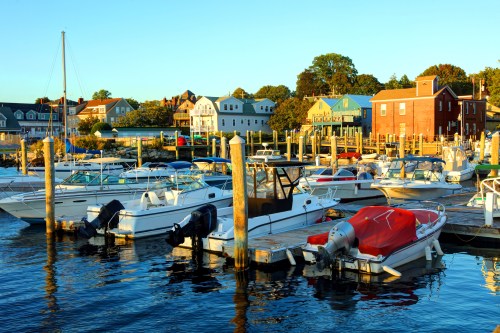 A marina at sunset with various boats docked and colorful houses in the background.