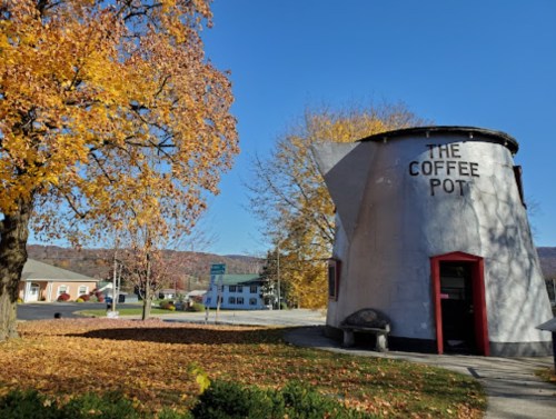 A quirky coffee pot-shaped building surrounded by autumn trees and a clear blue sky.