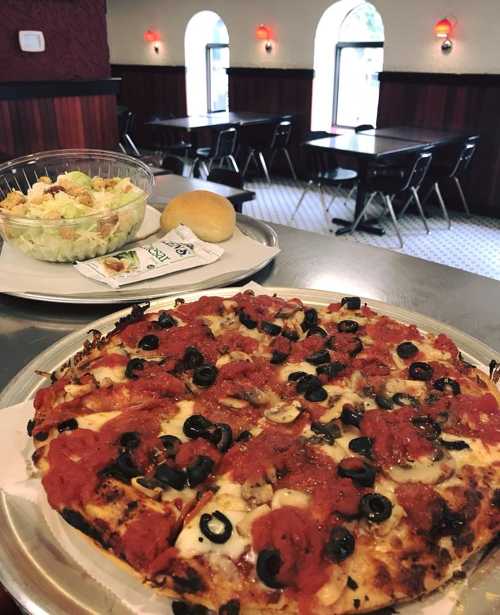 A pizza topped with sauce, olives, and cheese, served with a side salad and a roll in a cozy restaurant setting.