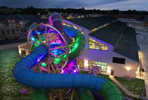 A colorful water slide with vibrant lights next to a modern building, set against a twilight sky.