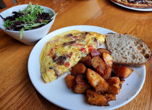 A plate with a vegetable omelet, roasted potatoes, a slice of bread, and a side salad in a bowl.